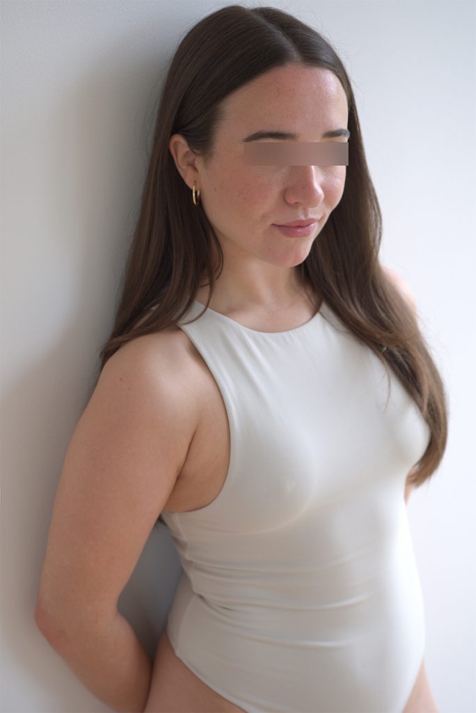 escort girl sofia in einem weißen body lehnt an der wand